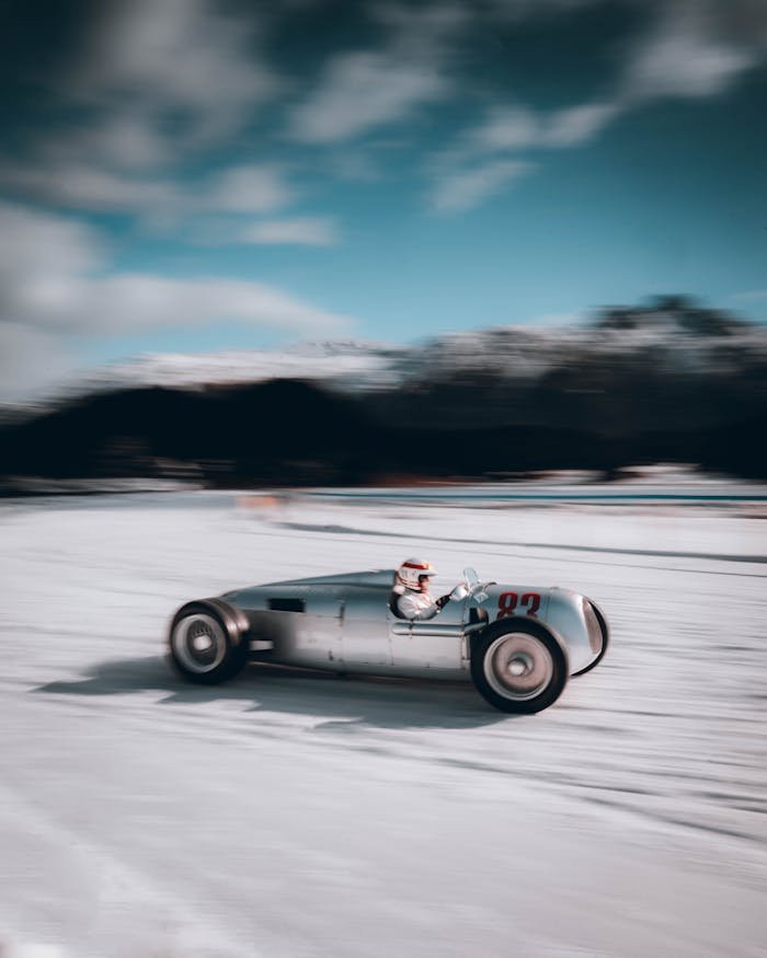 A historic racing car speeds on a snowy track during a winter race, capturing the thrill of vintage motorsport.