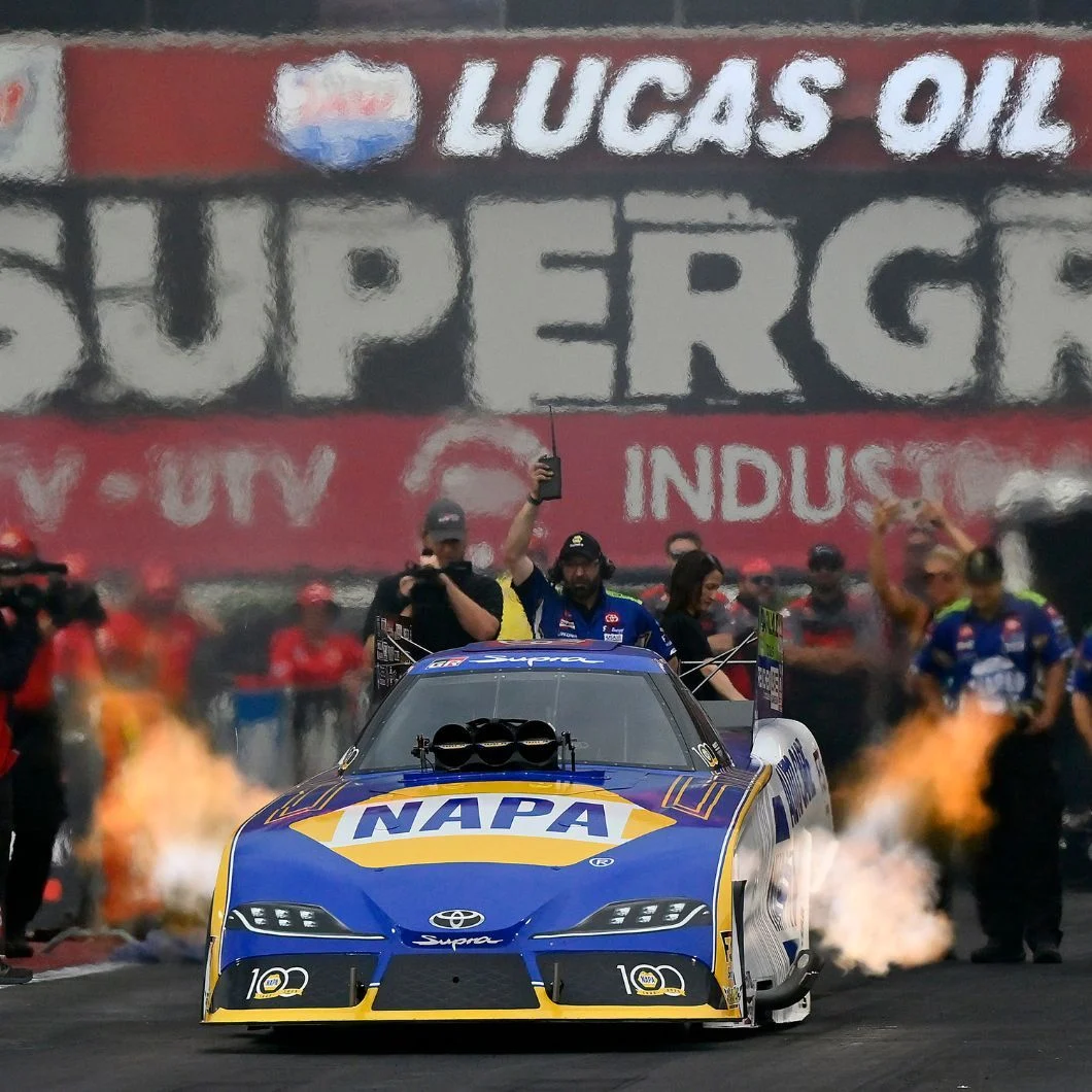 NHRA Funny Car launching off the starting line with smoke and flame at a drag racing national event