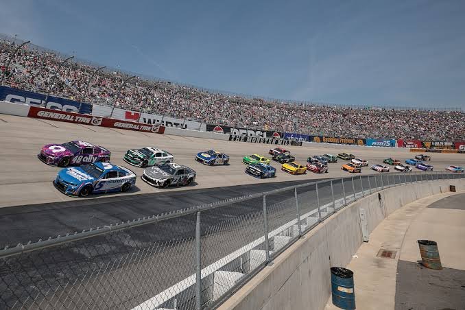 NASCAR Cup Series cars racing three-wide on the high banks of Dover Motor Speedway