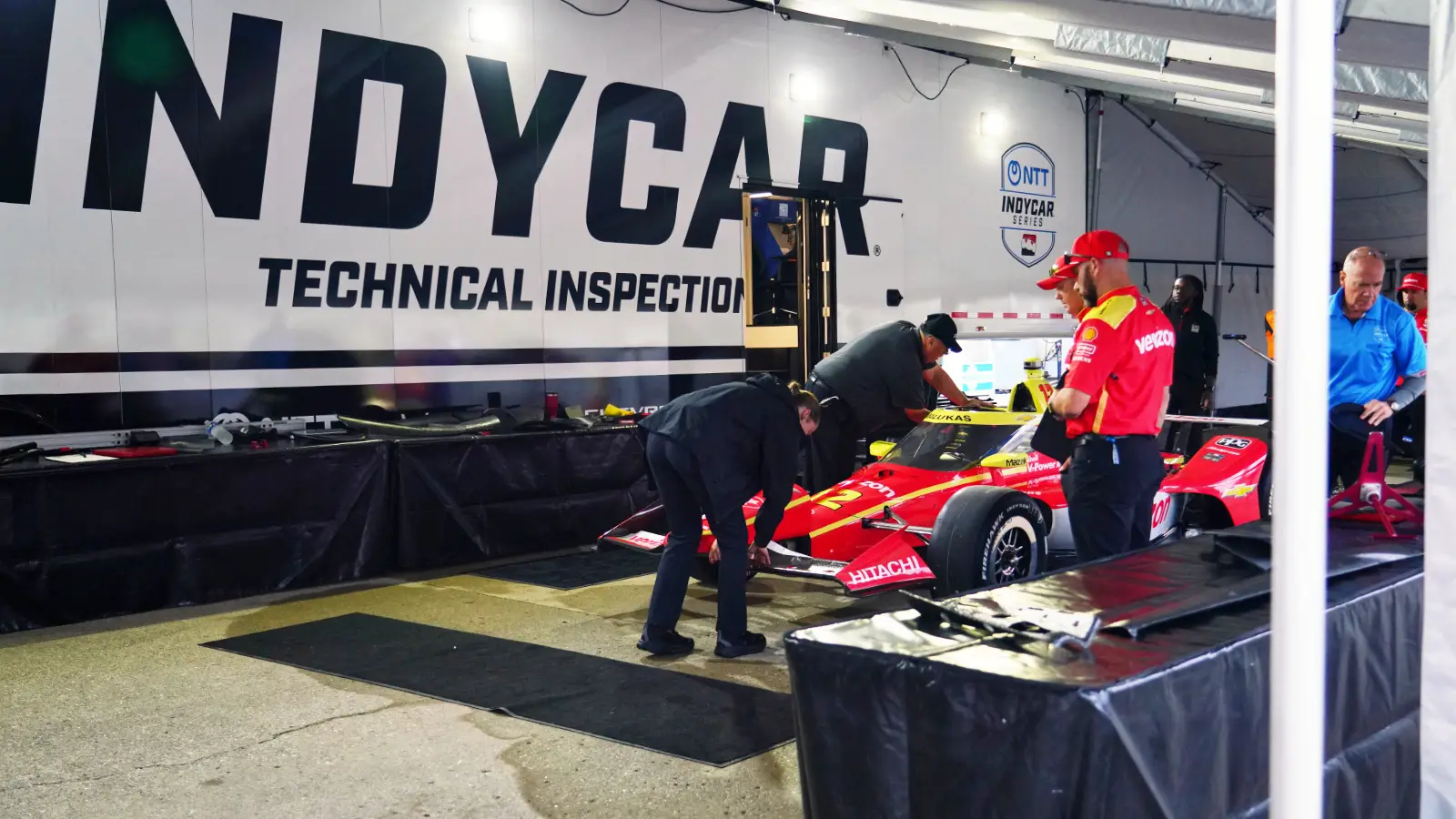 Racing mechanics working on an open-wheel race car powertrain in the IndyCar paddock
