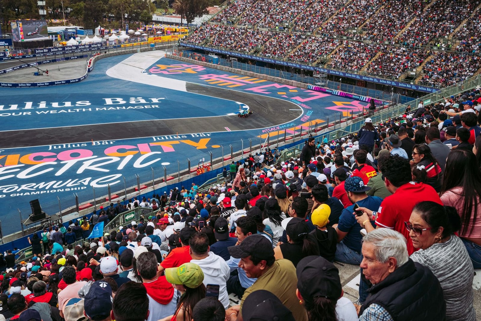 Formula E race cars on a temporary city street circuit at twilight — grandstand crowds watching close wheel-to-wheel racing under circuit lighting