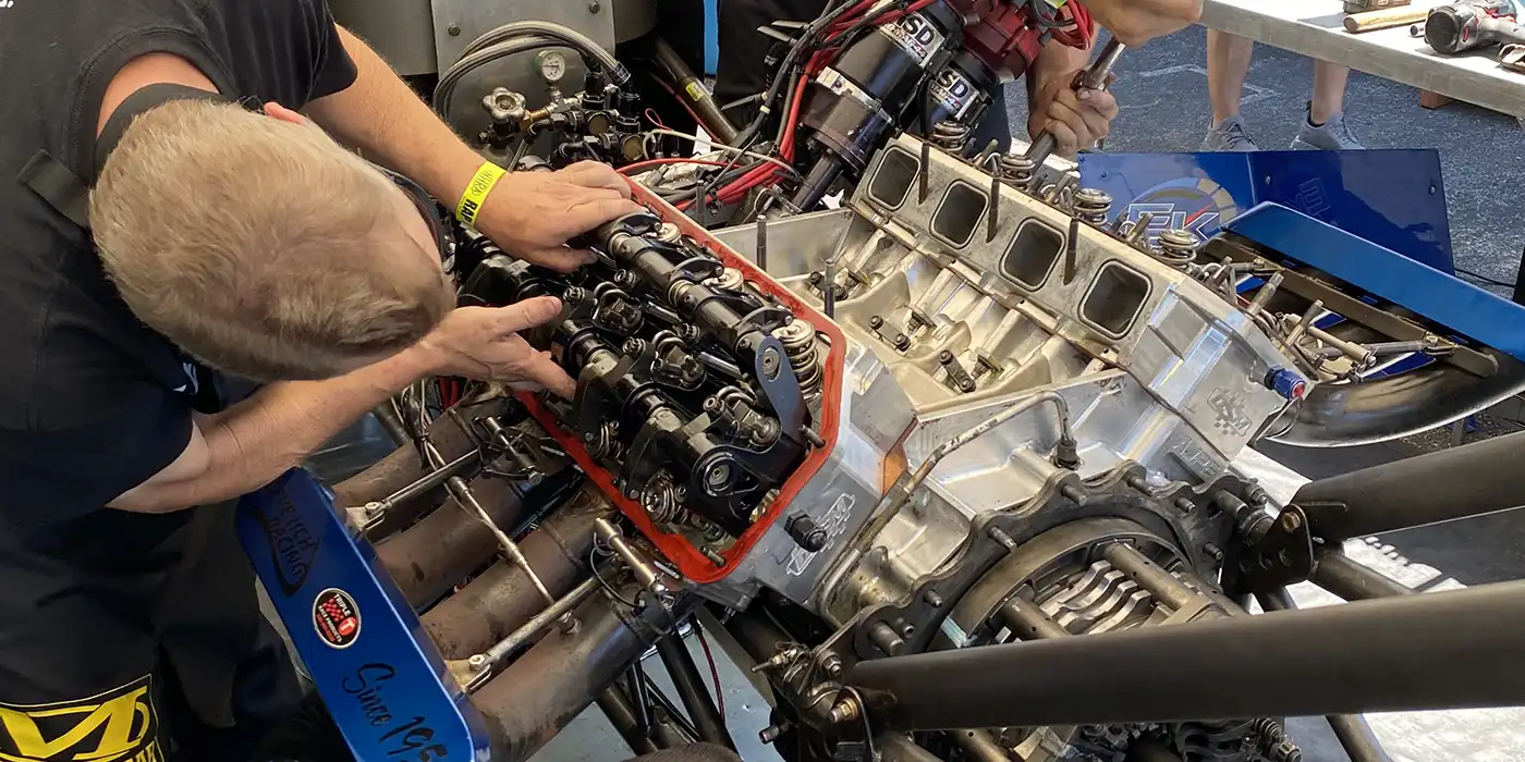 NHRA Funny Car body tilted up exposing the supercharged engine at a national event pit lane