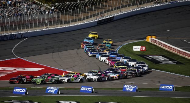 Aerial view of NASCAR Cup Series cars racing on a D-shaped intermediate oval speedway