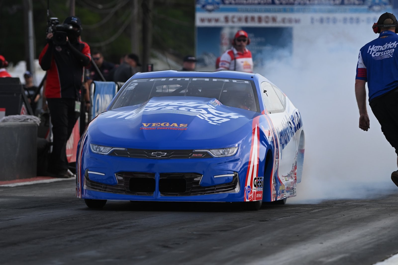 NHRA Pro Stock drag racing car launching from the staging area with front wheels lifting
