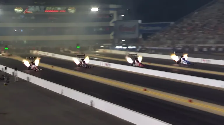 NHRA Top Fuel dragster racing down the track at high speed with parachute deployed at the finish