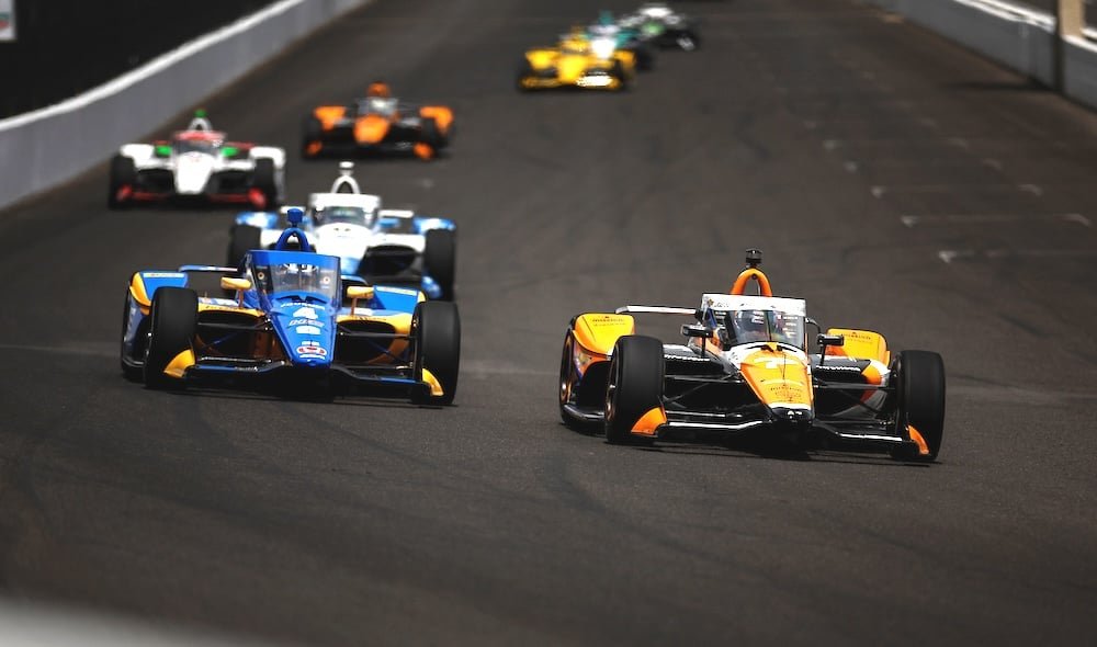 IndyCar open-wheel race car running at speed on a road course showing the current 2.2-litre hybrid V6 powertrain