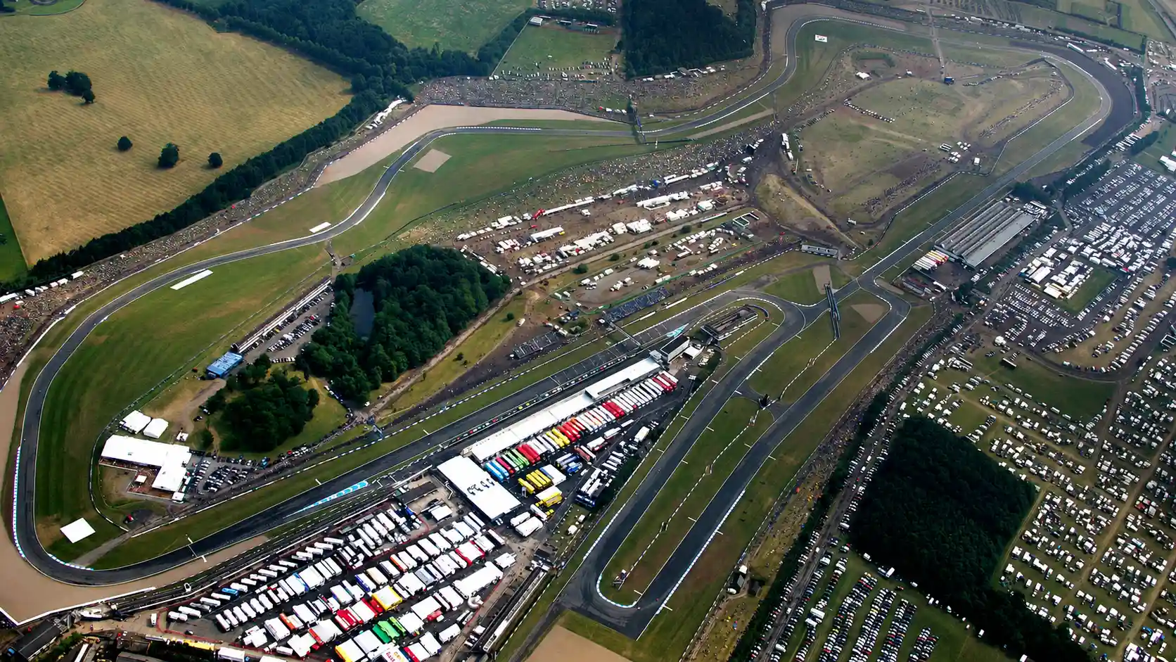 Racing motorcycles at speed through a flowing corner sequence with grandstands and spectators visible representing the Donington Park WorldSBK atmosphere