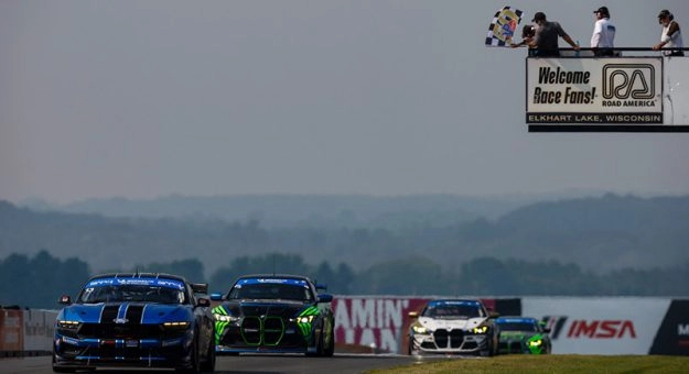 IMSA Michelin Pilot Challenge cars racing beneath the Road America welcome sign