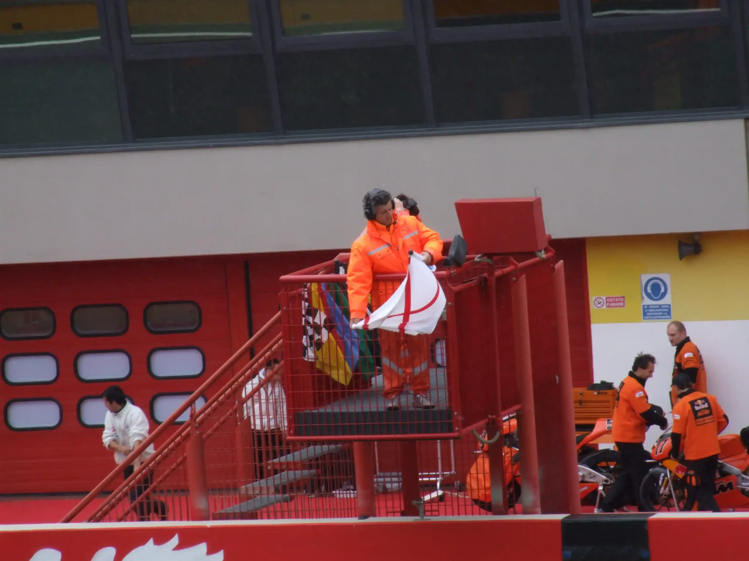 Marshal displaying a yellow-and-red striped slippery-surface flag during 2006 Formula 1 testing at Mugello