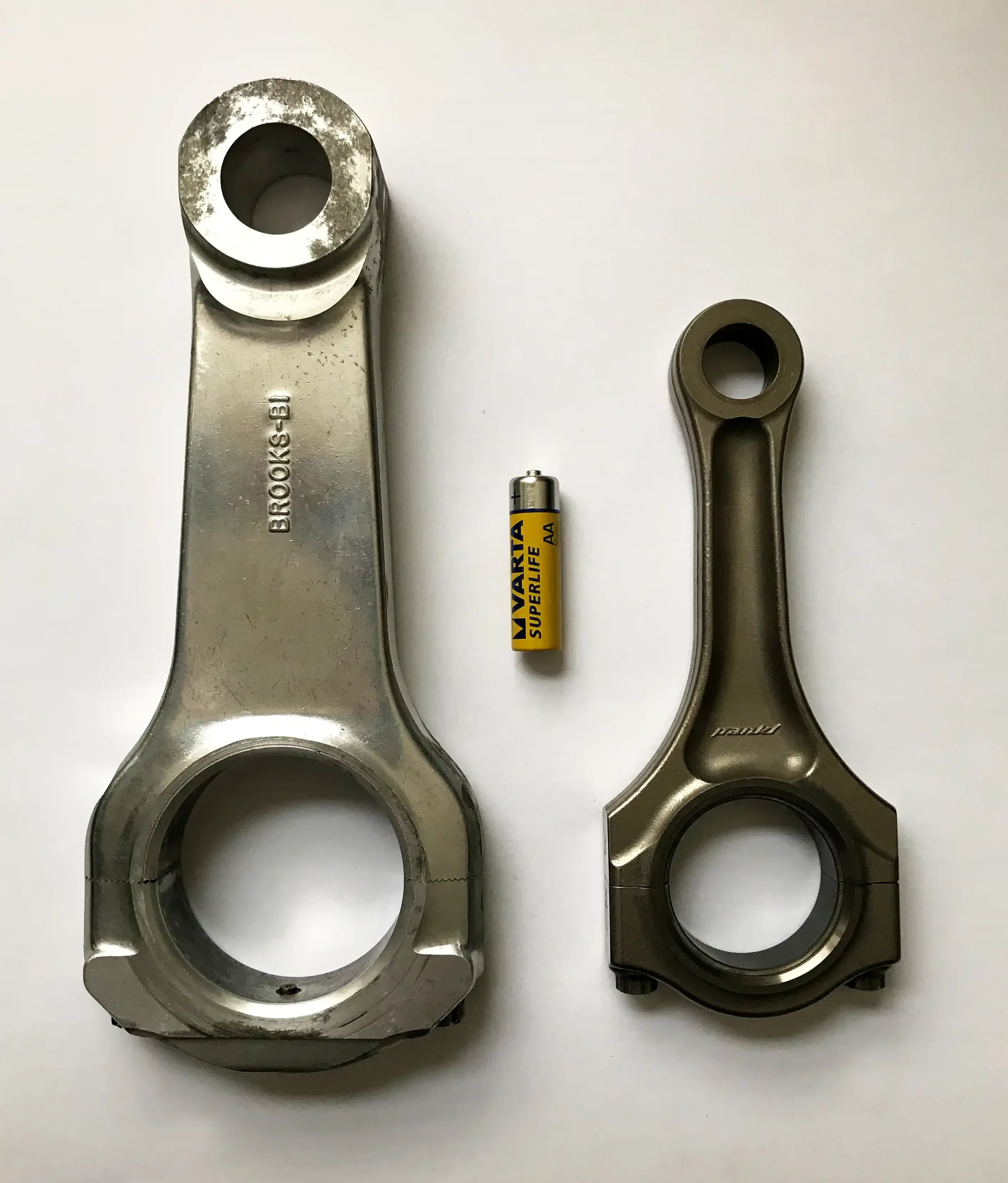 Top Fuel dragster connecting rod beside a Ferrari 458 connecting rod and AA battery for scale