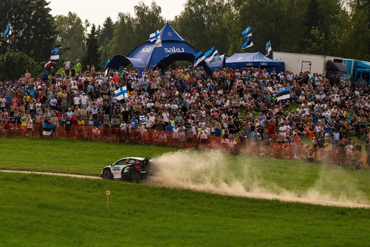 Rally car racing past large crowds and Estonian flags at WRC Rally Estonia