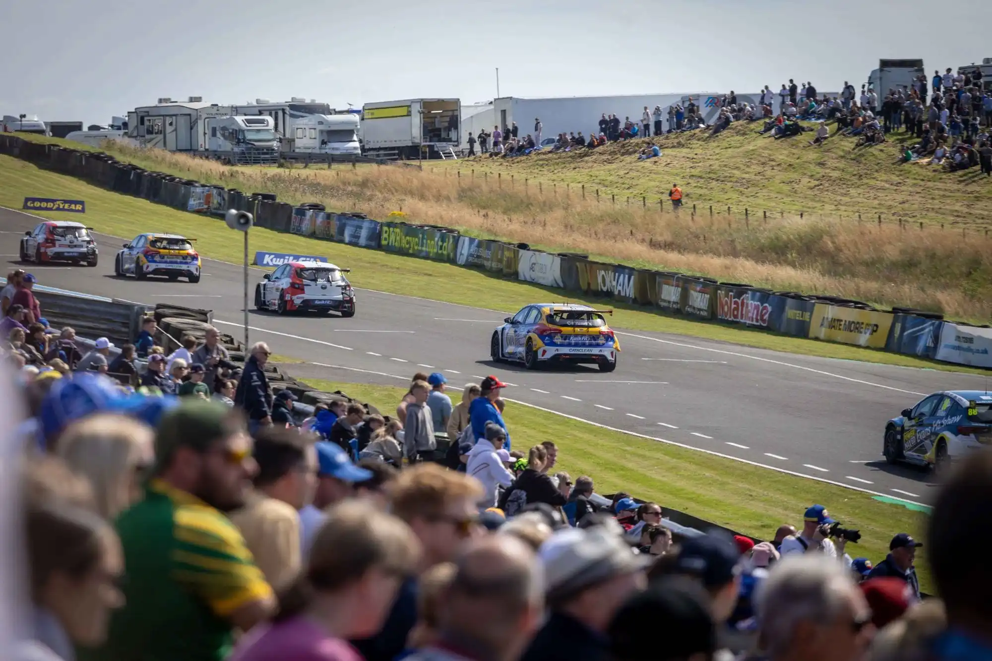BTCC race cars accelerating along the straight at Knockhill with spectators watching